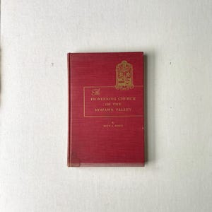 May include: A red hardcover book with gold lettering titled "The Pioneering Church of the Mohawk Valley" by John F. Rieh