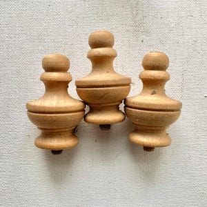 May include: Three unfinished wooden finials with a turned design. Each finial has a rounded top, a bulbous middle section, and a smaller base. The wood has a light, natural color, and the finials are arranged against a neutral background.