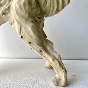 May include: A close-up of a cream-colored sculpture of an animal's leg and lower body. The sculpture has a textured surface with dark blue spots and the word "ITALIA" is visible on the leg.