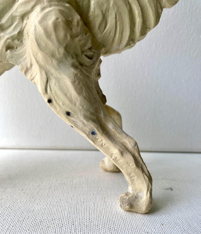 May include: A close-up of a cream-colored sculpture of an animal's leg and lower body. The sculpture has a textured surface with dark blue spots and the word "ITALIA" is visible on the leg.