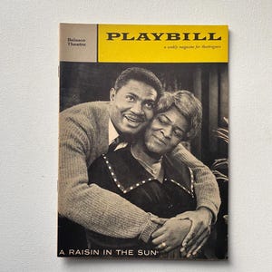 May include: Vintage Playbill magazine cover for "A Raisin in the Sun." The cover features a black and white photo of a man and woman embracing. The magazine title "PLAYBILL" is in yellow, with the Belasco Theatre logo.