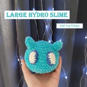 Puede incluir: Un juguete de peluche azul tejido a crochet con forma de mancha con ojos blancos y azules. El juguete está etiquetado como "LARGE HYDRO SLIME PDF PATTERN".