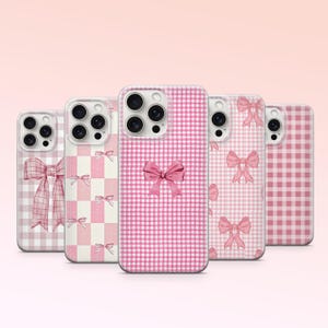 Pode incluir: Cinco capas para iPhone em vichy rosa e branco com um design de laço rosa. As capas são todas transparentes e mostram a lente da câmera do telefone.