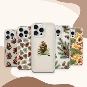 May include: Five clear phone cases with different designs. The cases feature pine cones, pine branches, and a combination of pine cones and branches. The cases are all for the iPhone 14 Pro Max.