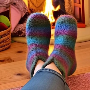 Może przedstawiać: Paski kapci w kolorach niebieskim, fioletowym i zielonym. Skarpetki są noszone w pomieszczeniach, z kominkiem w tle. Skarpetki wydają się być ręcznie robione i są wygodnym, ciepłym dodatkiem.