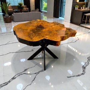 Könnte beinhalten: Einzigartiger Couchtisch mit einer Tischplatte aus Naturholz mit lebendiger Kante und einem geometrischen schwarzen Metallgestell. Die Tischplatte hat einen warmen, goldenen Farbton mit dunklen Kanten, was einen auffälligen Kontrast erzeugt. Ein Möbelstück.