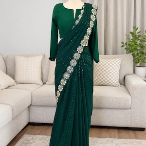 May include: A dark emerald green saree with intricate floral embroidery along the border and a matching long-sleeved blouse. The saree is draped on a mannequin, showcasing its elegant design and texture. The blouse has a keyhole neckline.