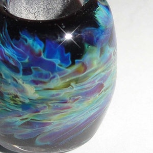 May include: A dark blue glass bead with iridescent swirls of teal, green, and purple. The bead has a glossy finish.