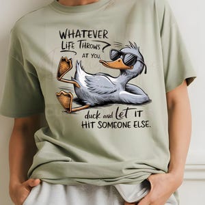 May include: Sage green t-shirt with a cartoon duck wearing sunglasses and the text "WHATEVER LIFE THROWS AT YOU, duck and let it HIT SOMEONE ELSE." The duck is lying down with its feet up.