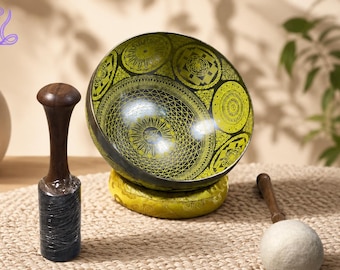 May include: A lime green and black singing bowl featuring intricate geometric and circular patterns, resting on a yellow cushion. The set includes a dark wooden mallet with a black base and a separate wooden mallet with a white felt ball tip.