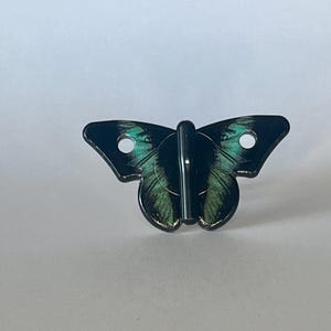 May include: Black butterfly-shaped hook with green and black wings. The hook is made of metal and has a silver finish.