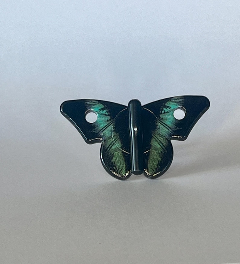 May include: Black butterfly-shaped hook with green and black wings. The hook is made of metal and has a silver finish.