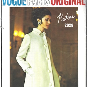 May include: A white coat with a button closure and a collar. The coat is photographed on a model with dark hair and a pearl earring. The text "Vogue Paris Original Patou 2029" is printed on the image.