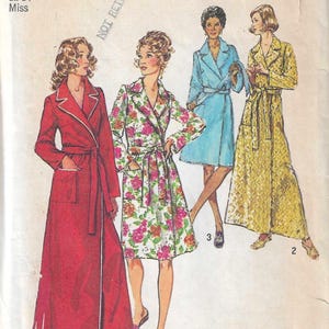 May include: A Simplicity 5989 sewing pattern envelope for a robe in medium size 12-14. The illustration shows four variations of a belted robe: a long red robe with white trim, a floral print knee-length robe, a short blue robe, and a long yellow robe.