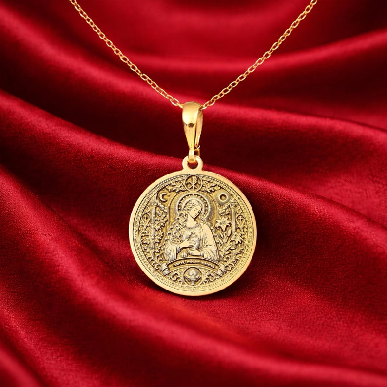 Gold Mary Magdalene necklace featuring Byzantine-inspired Christian iconography with radiant halo, sacred vessel symbolism, Chi-Rho emblem, floral ornamentation, and devotional engraved details on circular medallion pendant. Religious jewelry inspired by Orthodox iconography, medieval illuminated manuscripts, Renaissance saint portrait traditions, and sacred feminine symbolism. Christian pendant representing spiritual devotion, divine grace, resurrection, contemplation, sacred memory.