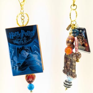 May include: Two gold-toned keychains featuring Harry Potter-themed charms. One keychain displays a miniature book cover of "Harry Potter and the Order of the Phoenix." The other has various charms, including a picture of Harry Potter and a building scene, with decorative beads.