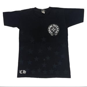 May include: Black t-shirt with a star pattern and a white logo on the chest pocket. The logo features the words "Chrome Hearts" in a circular design. The letters "CH" are printed in white on the lower left side.