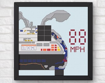 May include: Framed cross-stitch art featuring a DeLorean time machine design. The artwork includes the text "OUTATIME" and "88 MPH" in a pixelated style, set against a light blue background. The frame is black.