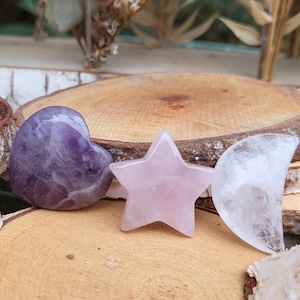 Könnte beinhalten: Drei polierte Kristallsteine in Form eines Herzens, eines Sterns und eines Halbmondes. Das Herz ist aus Amethyst, der Stern aus Rosenquarz und der Mond aus klarem Quarz. Die Steine liegen auf einer Holzoberfläche.