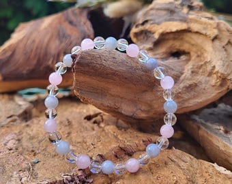 May include: A beaded bracelet featuring a mix of pink, clear, and gray gemstone beads. The bracelet is strung on a clear elastic cord. The beads are round and smooth, creating a delicate and elegant piece of jewelry.