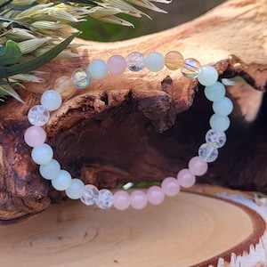 Puede incluir: Un brazalete hecho con cuentas de color azul claro, rosa y transparente. Las cuentas están enhebradas en un cordón elástico transparente.