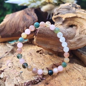 Könnte beinhalten: Ein mehrfarbiges Perlenarmband mit rosa, grünen, gelben und klaren Perlen. Das Armband besteht aus natürlichen Steinen und liegt auf einem Stück Holz.