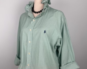 Puede incluir: Una camisa a cuadros verde claro y blanco con cuello con volantes y mangas enrolladas. La camisa presenta un pequeño logotipo azul marino en el pecho. Se ve un collar de cuentas negro.