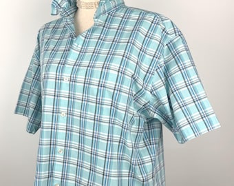 Puede incluir: Camisa de manga corta a cuadros azules y blancos con cuello con volantes. La camisa tiene cierre de botones y un corte relajado. La tela es probablemente ligera, adecuada para climas cálidos.