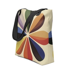 Puede incluir: Bolso tote de color crema con un estampado floral colorido. El diseño presenta una gran flor con pétalos en tonos naranja, rojo, amarillo, azul y morado. Tiene correas negras.