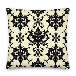 Puede incluir: Una almohada de color crema con un patrón damasco negro. El patrón presenta intrincados diseños florales y remolinos.