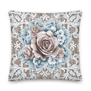 Puede incluir: Una almohada decorativa con un diseño floral. La almohada presenta un gran ramo de rosas en tonos marrones y azules, sobre un fondo de patrón damasco blanco y marrón.
