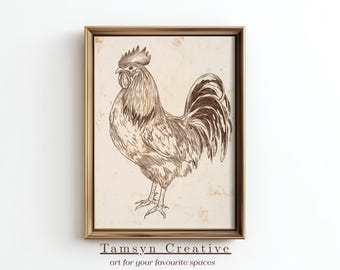 May include: Framed artwork featuring a detailed pen and ink illustration of a rooster. The rooster is depicted in shades of brown against a beige background, with a gold-colored frame. The text "Tamsyn Creative" and "art for your favourite spaces" is at the bottom.