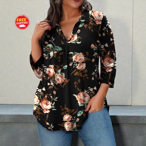 May include: Black floral print top with a V-neck and three-quarter sleeves. The top features a pattern of pink and peach roses with green leaves and brown stems. The shirt is paired with blue jeans.
