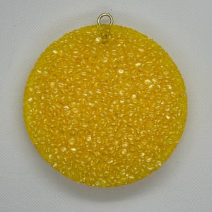 May include: A round, yellow ornament with a textured surface. The ornament has a gold loop at the top for hanging.