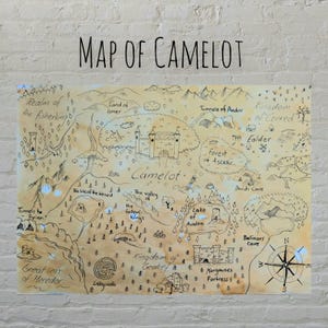 Puede incluir: Un mapa dibujado a mano de Camelot, un reino ficticio, con una brújula en la esquina inferior derecha. El mapa presenta varios lugares, incluyendo el Reino del pescador, la Tierra de Ismer, el Bosque de Ascetir, el Reino de Cenred y el Lago de Avalon.