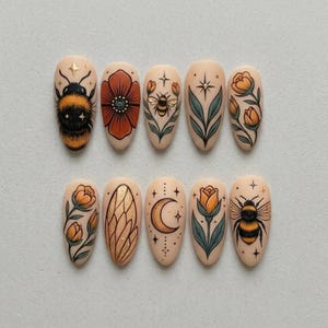 May include: A set of ten almond-shaped false nails with various designs. The designs include a bumblebee, a red poppy, a bee, a leaf, a flower, a gold wing, a crescent moon, and a star.