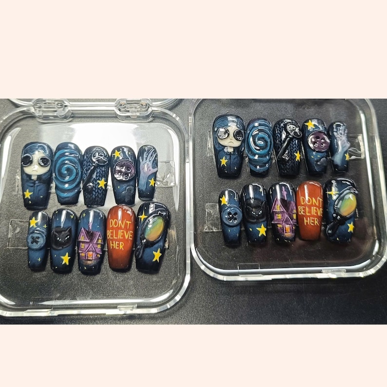 May include: A collection of press-on nails in dark blue and black. Each nail is decorated with individual artwork, including a character, swirling patterns, a house, and the text "DON'T BELIEVE HER". Yellow stars are used as accents.