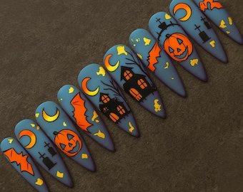 May include: A set of ten long, pointed, blue artificial nails with Halloween-themed designs. Each nail features orange and yellow illustrations of bats, jack-o'-lanterns, moons, and haunted houses. The nails are arranged on a dark surface.