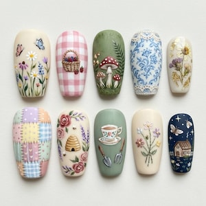 May include: A collection of ten painted artificial nails with various designs. The designs include floral patterns, gingham, mushrooms, a teacup, a beehive, and a small house. Colors include pastels, greens, and blues. The nails are arranged in a row.