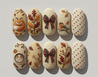 May include: A set of ten artificial nails with autumn-themed designs. The nails feature images of a fox, fall leaves, a plaid bow, a bird, and coffee art. The nails are beige with brown and orange accents.