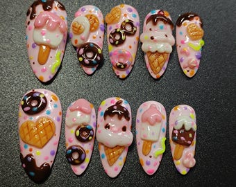 May include: A set of ten artificial nails, each painted light pink with colourful polka dots. Each nail features a 3D dessert design, including ice cream cones, ice lollies, and doughnuts with chocolate and pink frosting.
