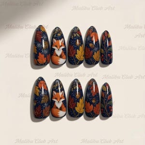 Könnte beinhalten: Set aus zehn ovalen Kunstnägeln mit dunkelblauem Hintergrund. Jeder Nagel zeigt herbstliche Designs, darunter orange und gelbe Blätter, einen Fuchs und Beeren. Die Nägel sind mit Glitzer verziert.