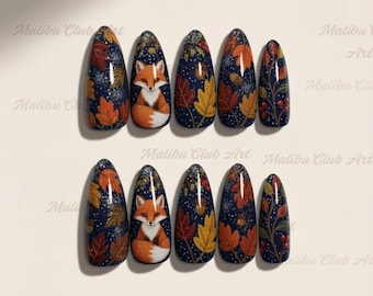 May include: Set of ten oval-shaped false nails with a dark blue background. Each nail features autumn-themed designs, including orange and yellow leaves, a fox, and berries. The nails are decorated with glitter.