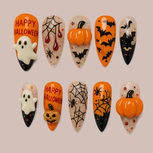 Puede incluir: Un conjunto de diez uñas postizas con temática de Halloween. Los diseños incluyen uñas naranjas con texto "Happy Halloween" y un fantasma, telarañas, calabazas y murciélagos. Las uñas son en forma de almendra con un acabado brillante.