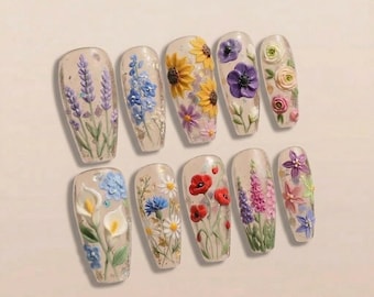 May include: A set of ten artificial nails, each adorned with a different 3D floral design. The designs include lavender, sunflowers, poppies, and other colorful flowers. The nails have a clear base with a glossy finish.