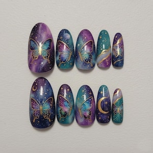 May include: A set of ten oval-shaped false nails. Each nail features a galaxy-themed design with a butterfly and gold accents. The color palette includes purple, blue, and teal, with a starry effect. The nails are arranged on a white surface.