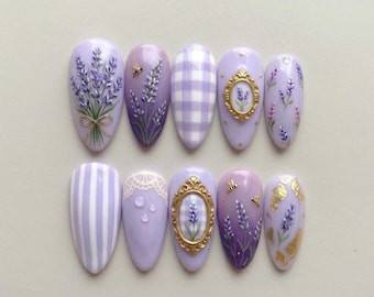 May include: A set of ten lavender-themed artificial nails. Designs include lavender bouquets, bees, gingham, gold frames, stripes, and gold leaf accents. The nails are oval-shaped and painted in shades of purple and white.