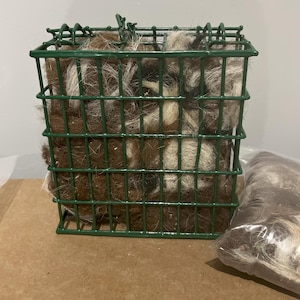 May include: A green wire cage filled with brown and white wool fibers. A separate bag of brown and white wool fibers is on the right side of the image.