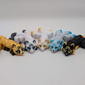May include: Six small, segmented, hand-painted figurines of foxes in various colors, including black, white, blue, and gold. Each figurine has a curled tail and a playful expression.