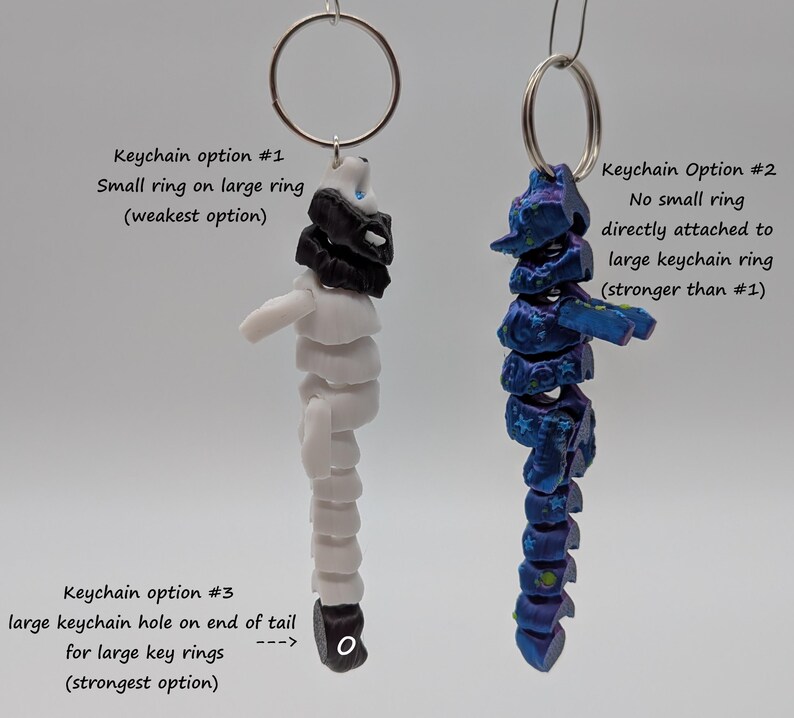 Op de afbeelding: Twee sleutelhangers met verschillende bevestigingsopties. De ene is wit en zwart, de andere blauw en paars. Tekst geeft de sterkte van elke optie aan: kleine ring aan grote ring, geen kleine ring en groot sleutelhangergat.